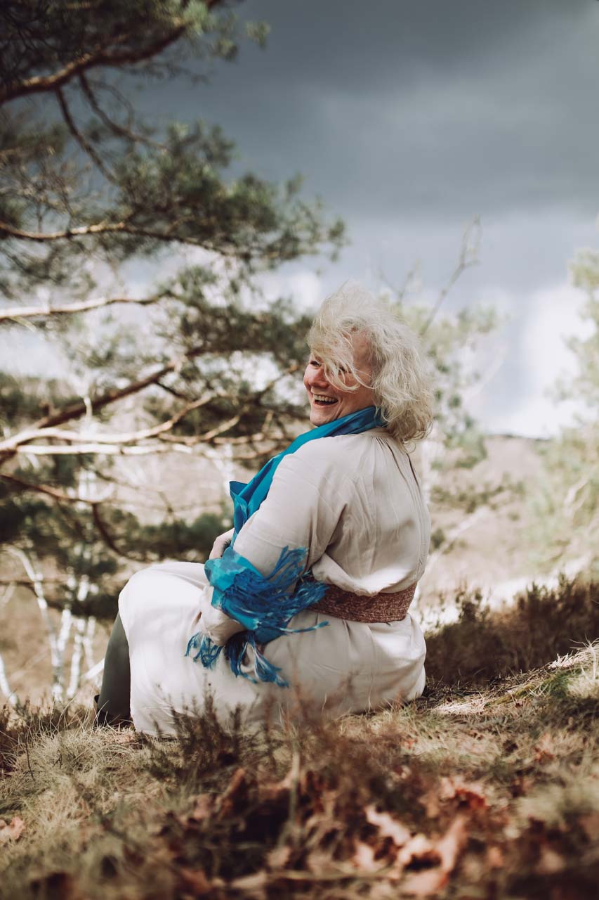 Astrid sitzt lachend in der Natur.